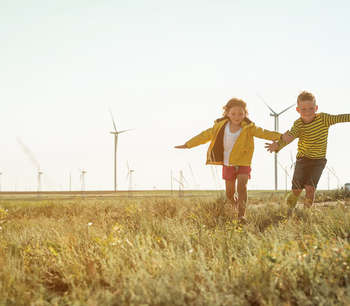ילדים רצים בשדה וברקע תחנות רוח